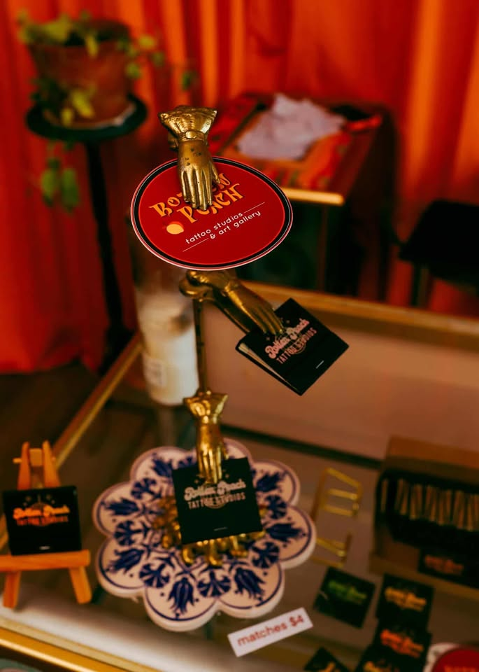 Rotten Peach Studios red-oval logo on a gold hand stand, with branded matchbooks and stickers